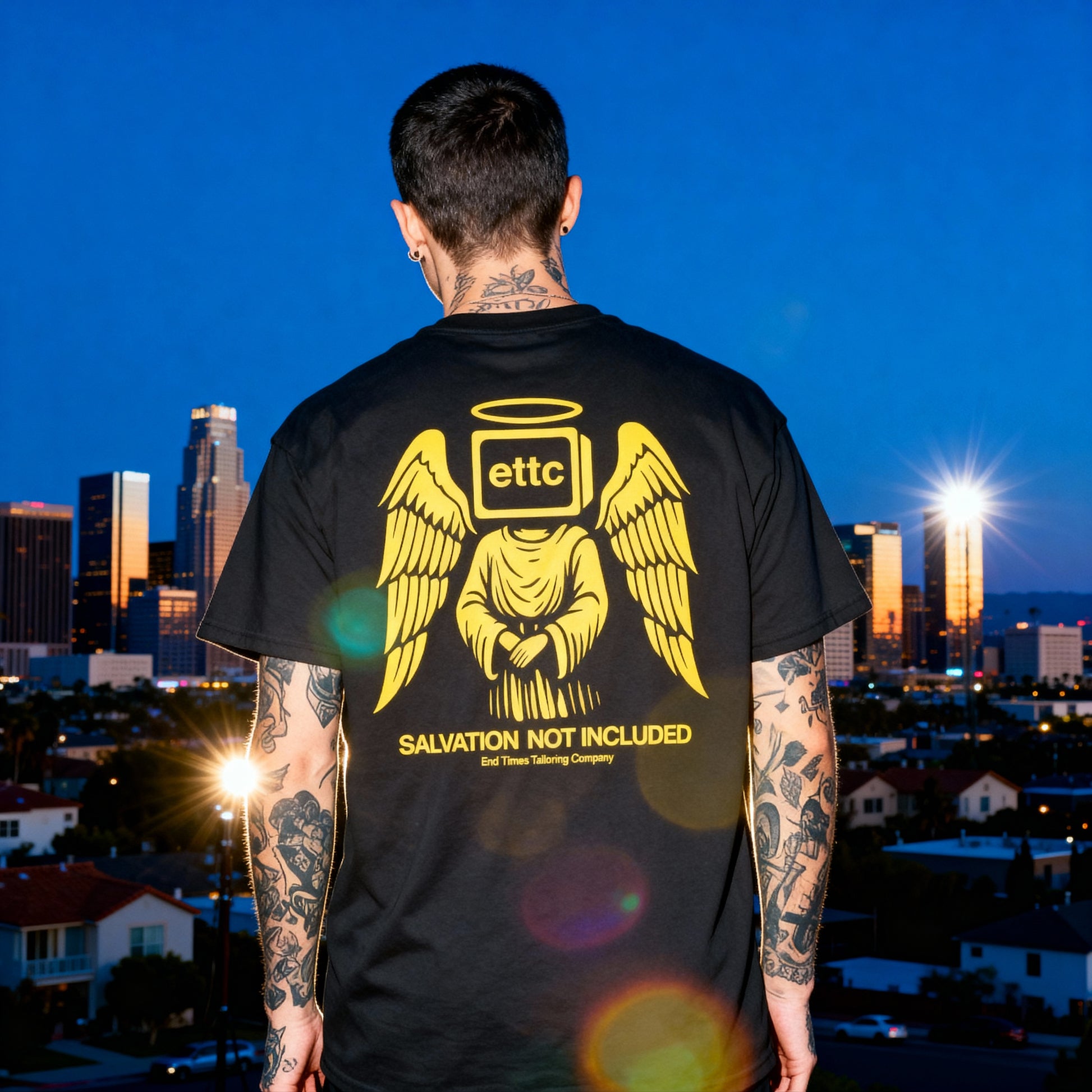 Person wearing a black t-shirt with a graphic design and text, standing against a city skyline at night.