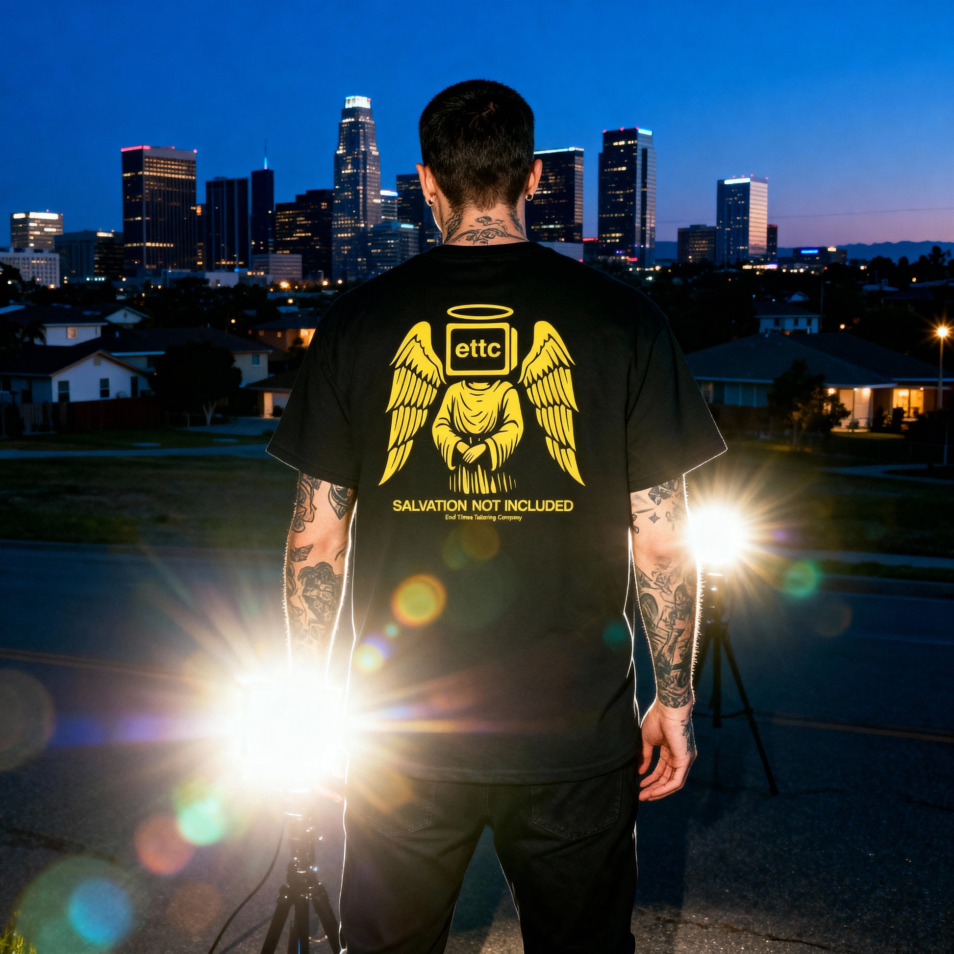 Person wearing a black t-shirt with a yellow graphic and text, standing against a city skyline at night.